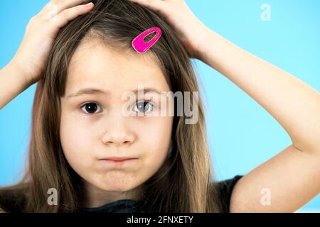 Close up portrait of upset and pensive little girl with cute pink hairpin on blue background. Stock Photo