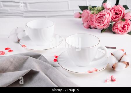 Two empty white cups for coffee and a bouquet of roses. Table setting for a morning breakfast for two. Stock Photo