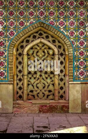 Wall with a pattern of ceramic tiles with an oval hole covered with a decorative lattice of carved yellow and pink marble  in the Golestan Palace. Stock Photo