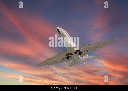 Airplane in the sky at sunrise or sunset. Small business jet is flying with lights and deployed landing gear preparing for landing or after takeoff Stock Photo