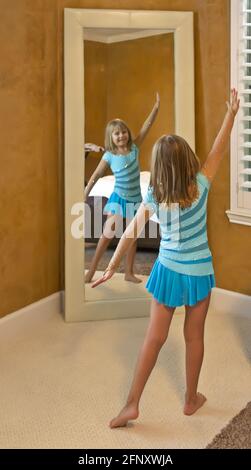 Young girl wearing ice skating dress practicing her pose in front of the floor mirror. Stock Photo