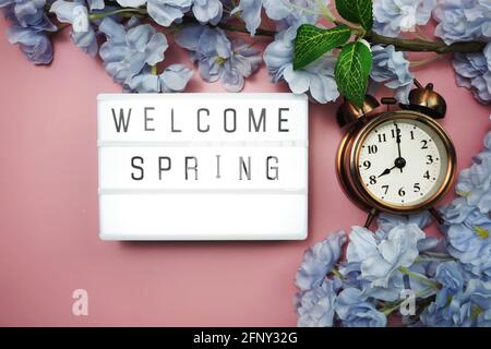 Welcome Spring text in light box and alarm clock with space copy on pink background Stock Photo