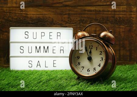 Summer Sale text in light box and alarm clock on wooden background Stock Photo