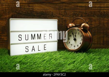 Summer Sale text in light box and alarm clock on wooden background Stock Photo