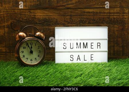 Summer Sale text in light box and alarm clock on wooden background Stock Photo