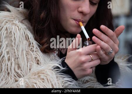A woman light a cigarette as people sit on outside terraces to have a  drink, in Paris, on May 19, 2021 as cafes, restaurants and other businesses  re-opened as part of an easing of the nationwide lockdown due to the  Covid-19 pandemic. The French made 