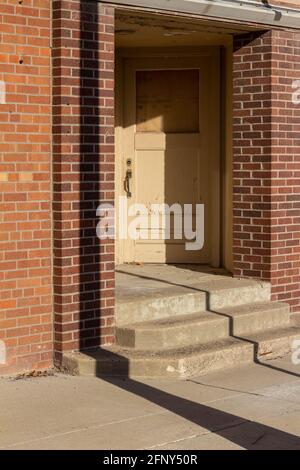 Close up view of an indented and angled vintage yellow entry door on an antique red brick urban building in sunlight Stock Photo