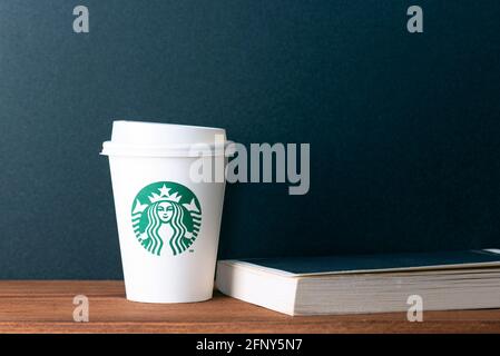 BERLIN - MAY 19: Paper white cup with Starbucks logotype and book on wooden table in Berlin, May 19. 2021 in Germany. Stock Photo