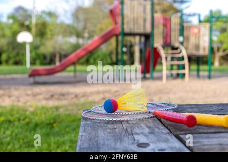 Badminton game rackets and shuttlecock on wooden table and children playground in the backgroud in the park on a sunny summer day. Active lifestyle co Stock Photo