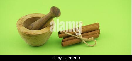 Wooden mortar and pestle near cinnamon sticks bundle tied with jute string over green background and free copy space for text Stock Photo