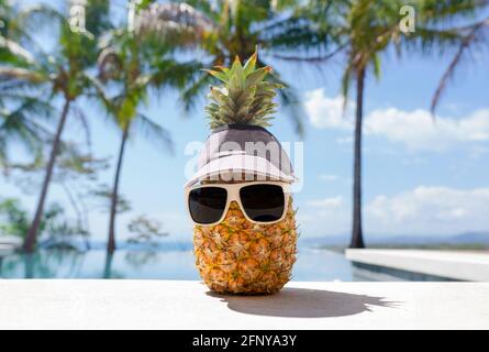 Funny pineapple character wearing sunglasses and a cap by a swimming pool on a tropical vacation Stock Photo