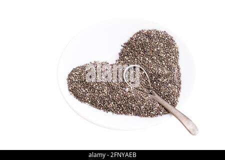 Heart symbol made of chia seeds and a tiny steel spoon on a white plate isolated on white Stock Photo