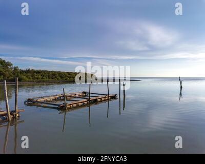 Scenic seascape view of a kelong stage on the sea with mangrove forest and blue sky background. Reflection on water Stock Photo