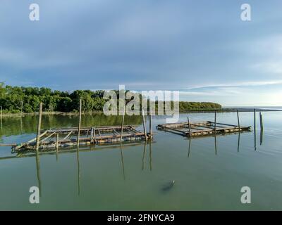 Scenic seascape view of wooden kelong stage on the sea with mangrove forest and blue sky background. Reflection on water Stock Photo