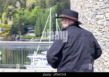 man on harbor pier over water wearing black denim jacket and hat Stock Photo