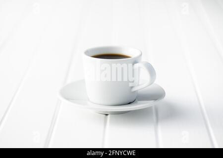 Black coffee in white mug on white wooden table. Stock Photo