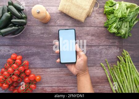 top view of man's hand holding smart phone with fresh vegetable on table  Stock Photo