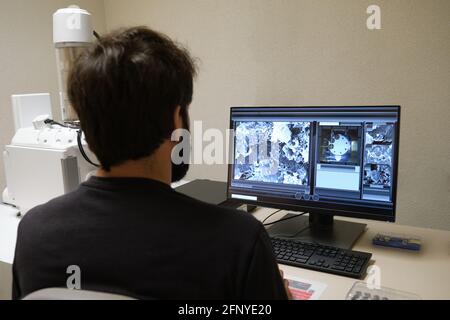 Young man scientist working with scanning electron microscope. Laboratory technician observing samples with a SEM. Stock Photo
