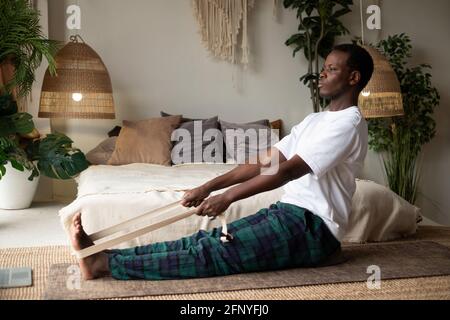 African young man sitting in paschimottanasana or Intense Dorsal Stretch pose, seated forward bend posture Stock Photo