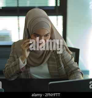 Portrait of young muslim businesswoman talking on the phone while working in office room Stock Photo