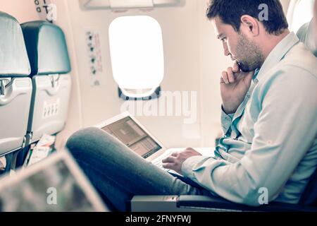 Businessman working with laptop on airplane. Stock Photo