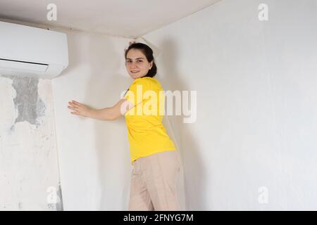 A woman repairman glues white wallpaper on the wall near the air conditioner under the ceiling Stock Photo