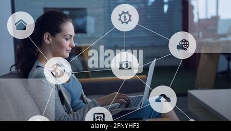 Composition of network of connections with icons over woman using laptop Stock Photo