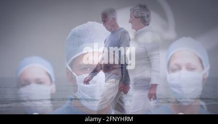 Senior couple waking on the beach against portrait of team of surgeons wearing face masks