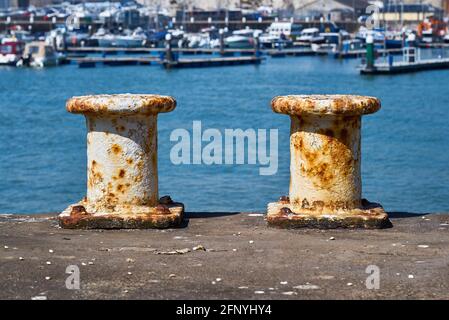 Two pillar bollards for mooring boats with the harbour in the background Stock Photo