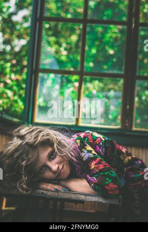 adorable girl with long blond hair lying on the table next to window Stock Photo