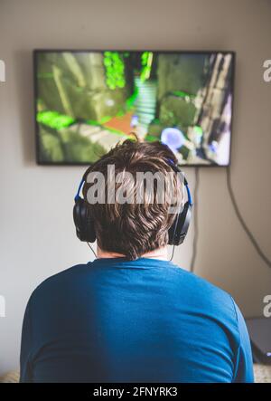 Rear view of a teenager staring at the television whilst playing video games and wearing microphone and headphones Stock Photo