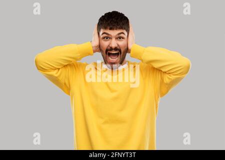 man in yellow sweatshirt closing ears by hands Stock Photo
