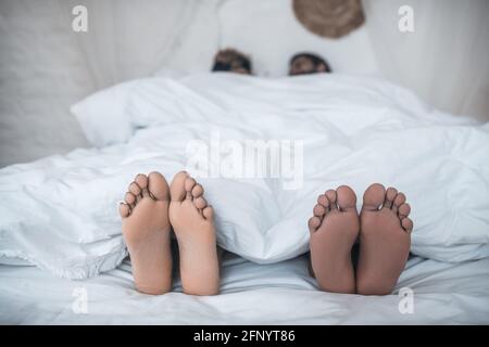 Husband and wife feet peeking out from under blanket Stock Photo