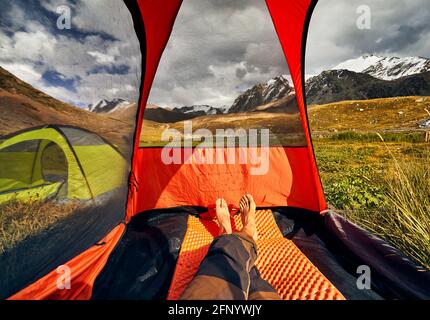 View from inside a tent and hikers legs on the mountains with glacier in Kazakhstan, Almaty Stock Photo