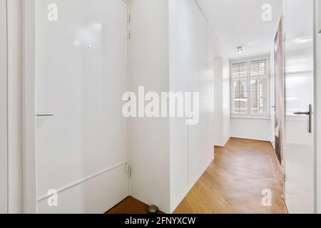 Interior design of narrow white hallway with shuttered window and doors leading to rooms in modern apartment Stock Photo