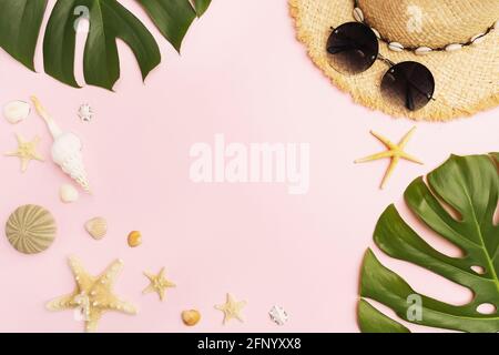Straw hat, sunglasses, seashells and monstera leaves on a pink background with copy space. Stock Photo