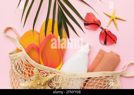 Beach accessories in a bag, sunglasses and a palm leaf on a pink background, summer background. Stock Photo