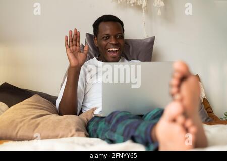 Black man with tablet resting in bed greeting waving hand. Stock Photo