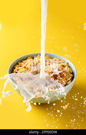 Pouring milk into bowl of corn flakes on yellow background Stock Photo