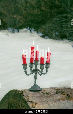 pewter candelabra with five red burning candles stands on a tree trunk outside in winter Stock Photo