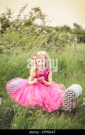 beautiful blond girl in pink dress in the meadow Stock Photo