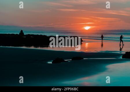 Sunset on the sea with some people wandering around on the beach, peoplle on the beach. Stock Photo