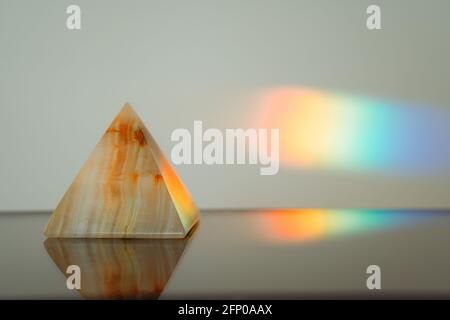 Agate pyramid with a rainbow streak background on a reflective surface Stock Photo