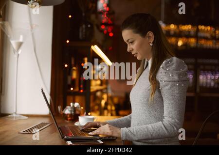The girl is in the premises of the cafe is typing a message on the computer. Remote work concept Stock Photo