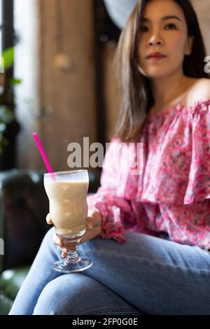 Pretty young asian woman drinking iced coffee in modern cafe.  Stock Photo