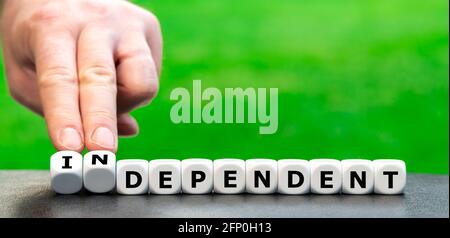 Hand turns dice and changes the word "dependent" to "independent". Stock Photo