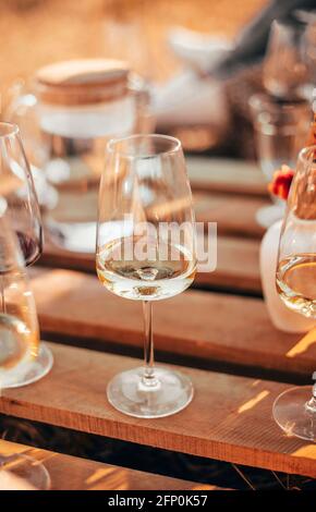 Set of elegant glassware placed on plank wooden table with floral arrangement on grassy meadow during festive autumn picnic Stock Photo