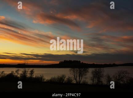 The sun starts to sink over the Hambleton peninsula on Rutland Water, as seen from the nature reserve near Manton. Stock Photo