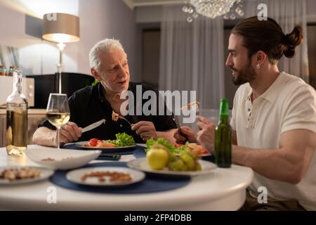 Elderly and young men chatting during dinner Stock Photo
