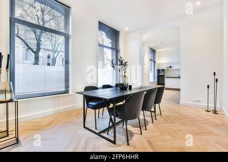 Luxury apartment dining room with parquet and black dining set against white kitchen in open plan house Stock Photo